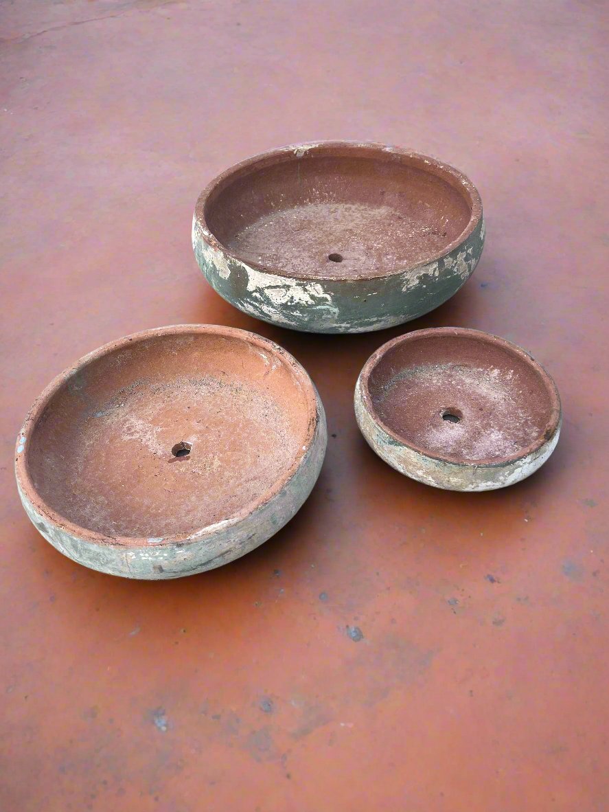 ancient green Vietnamese clay succulent garden bowls in three sizes on an old terracotta floor