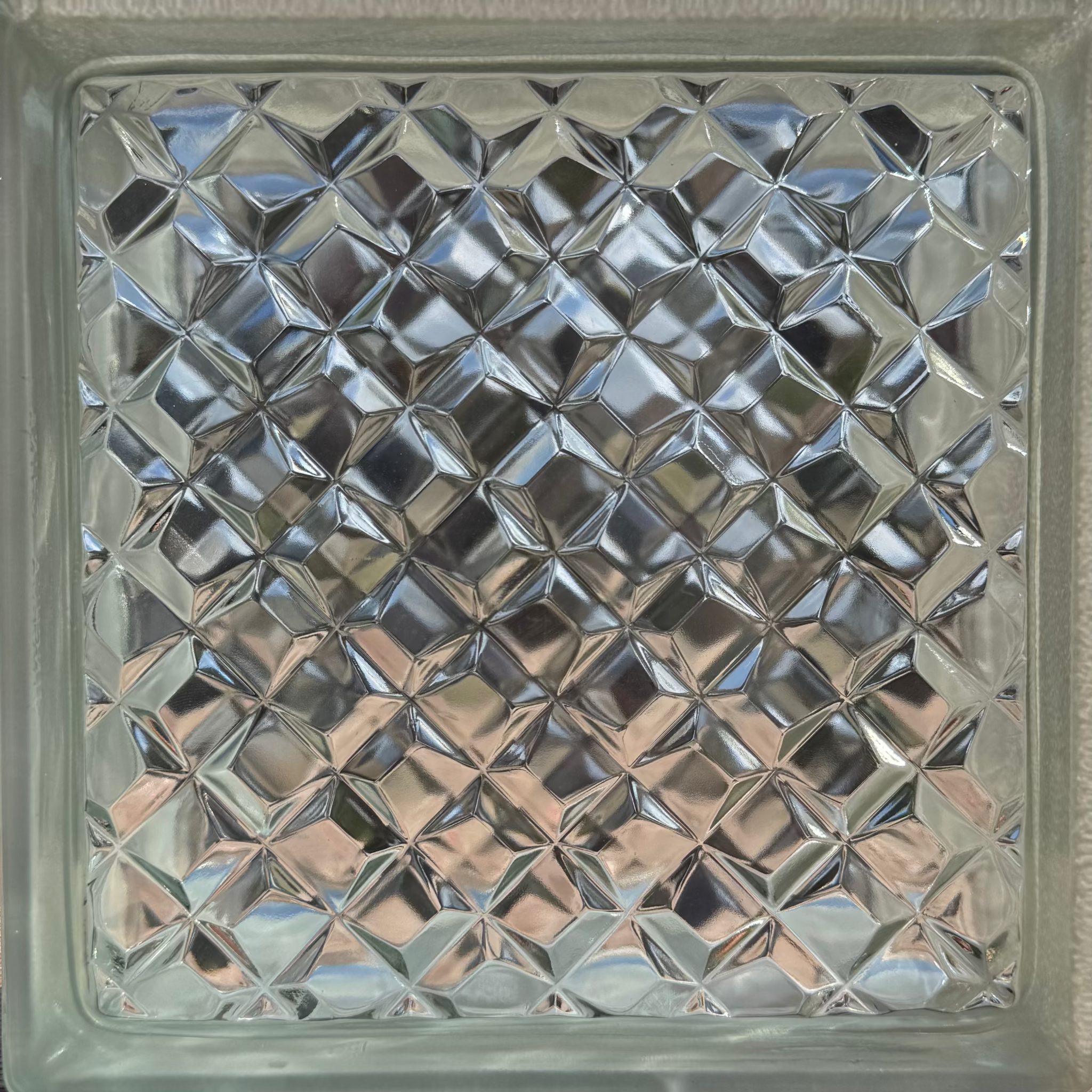 A square glass block featuring a textured, diamond-cut pattern on a clear glass surface.