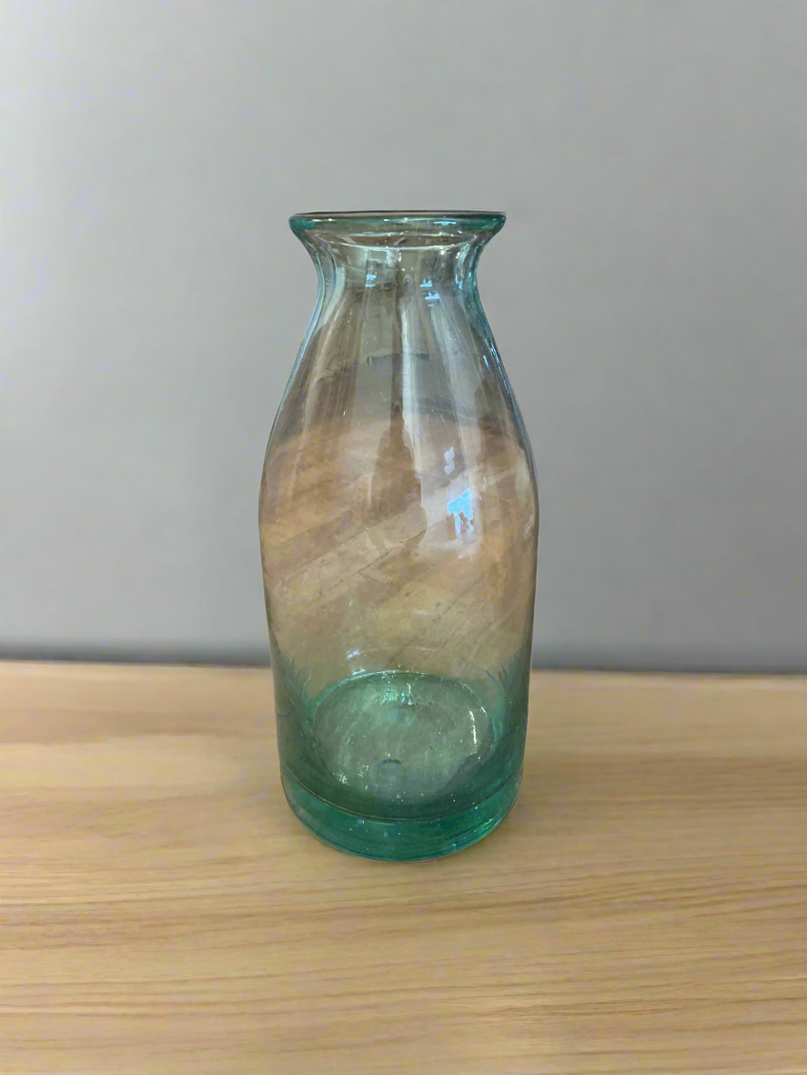 glass milk jug vase on wooden floor next to wall