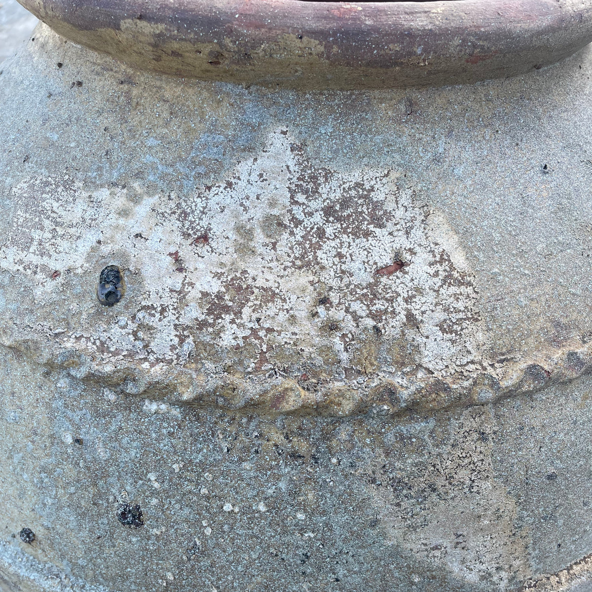 Close-up of a rustic ceramic pot or vase with a textured, weathered stone-like finish in gray, beige, and brown tones.