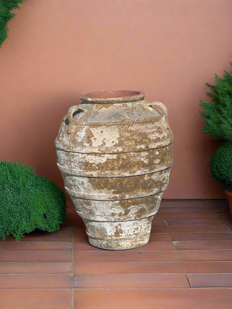 Ancient Ribbed Belly Urn with Handles and warn patina on terracotta tiles in front of a rendered wall