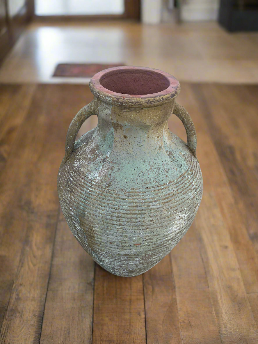 Two handle ribbed urn with warn patina inside on a wooden floor
