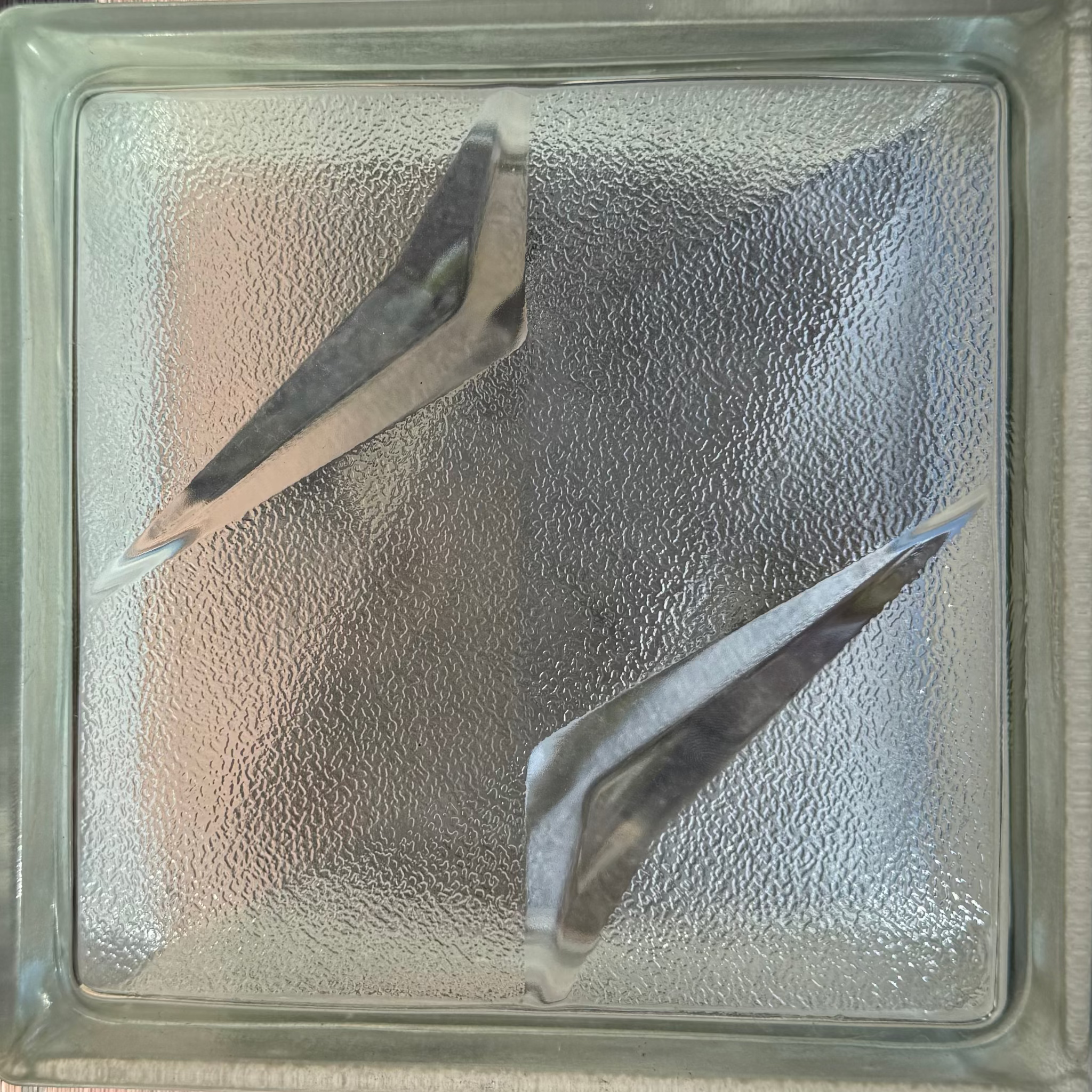 A square glass block door stopper or guard with a textured frosted glass center and two angled metallic glass wedge inserts, shown from a top-down perspective.